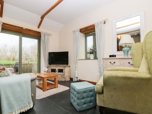 A living room with a television, a sofa, a chair, a coffee table, and a window with curtains. - Beech Cottage (Truro)