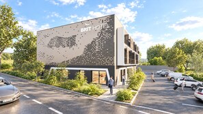 Un moderno edificio de hotel con un mural grande en la pared, un estacionamiento y huéspedes caminando.