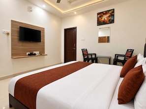 Ein Hotelzimmer mit Bett, Wandfernseher, Schreibtisch, zwei Stühlen und einer Tür.