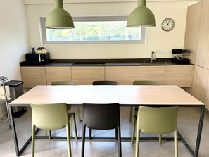 Ett modernt kök med ett stort bord, fyra stolar, ett fönster och en klocka på väggen.