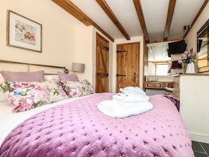 A bedroom with a bed, wooden doors, a dresser, and a television. - Oak Cottage (Truro)