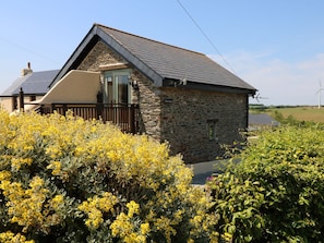 A stone cottage with a sloped roof, a visible chimney, and a small window. - Oak Cottage (Truro)