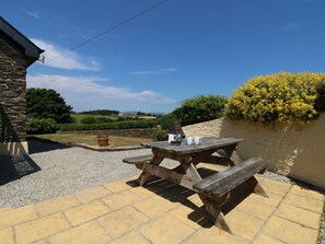 A wooden picnic table with a stone wall backdrop, a potted plant, and a clear view of a river and distant landscape. - Oak Cottage (Truro)