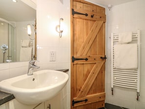 A bathroom with a white sink, a wooden door, a towel rack, and a shower. - Oak Cottage (Truro)