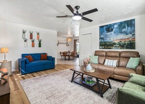 A living room with a blue sofa, a brown leather couch, a wooden coffee table, and a dining area with chairs and a table. - Heated Pool Retreat Near Manatees & Springs (Citrus Springs)