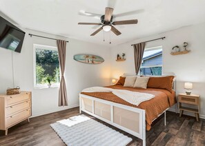 A bedroom with a bed, a nightstand, a dresser, a ceiling fan, a window with curtains, and a wall-mounted TV. - Heated Pool Retreat Near Manatees & Springs (Citrus Springs)