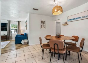 A dining area with a round table and six chairs, a blue sofa, and a large window with curtains. - Heated Pool Retreat Near Manatees & Springs (Citrus Springs)