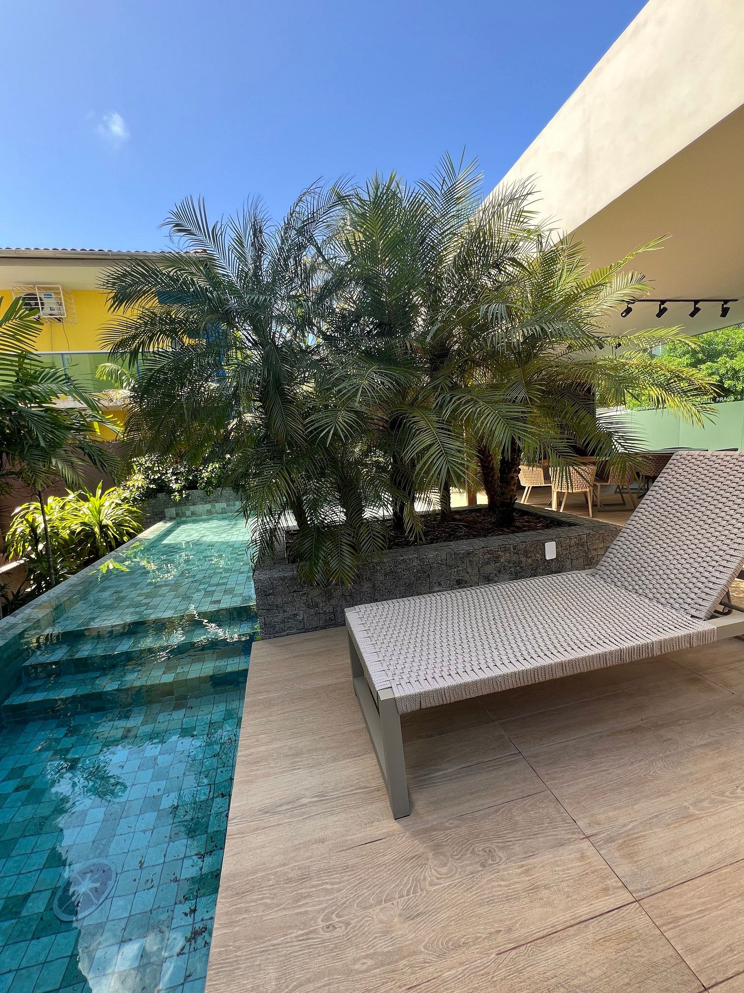 A pool area with a lounge chair and palm trees.