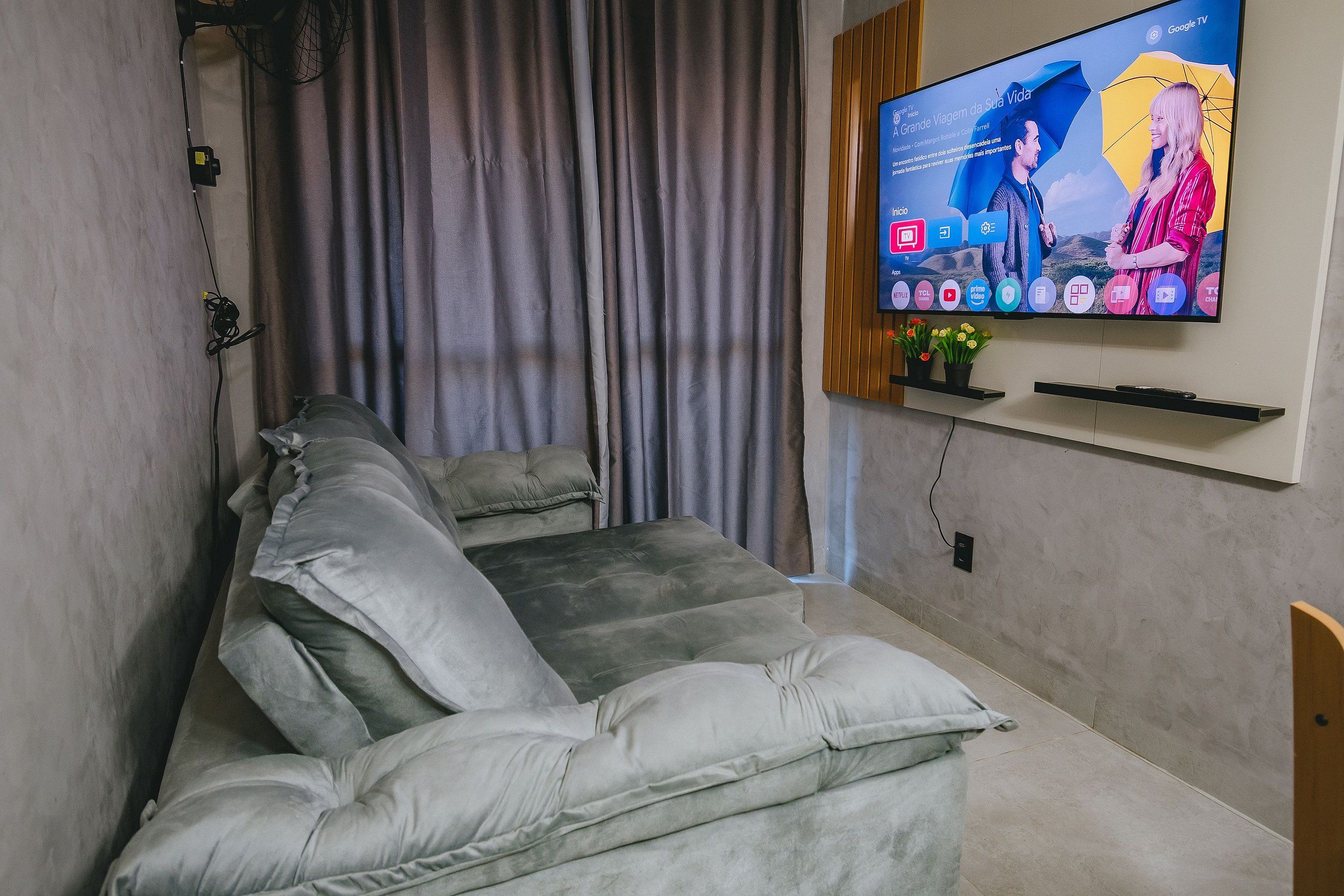 Una sala de estar moderna con un sofá gris, un televisor de pantalla plana montado en la pared y una cortina.