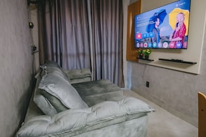 A modern living room with a gray sofa, a flat-screen TV mounted on the wall, and a curtain. - Praça 5 Ap. 103 Walter (Ipojuca)