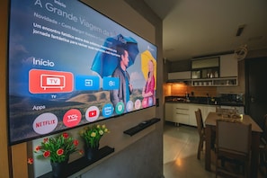 A modern living room with a large flat-screen TV mounted on the wall displaying various streaming services. - Praça 5 Ap. 103 Walter (Ipojuca)