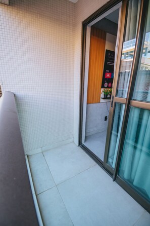 A hotel room with a tiled floor, a sliding glass door leading to a balcony, and a small indoor seating area with a TV and flower arrangement. - Praça 5 Ap. 103 Walter (Ipojuca)