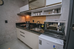 Cocina compacta con armarios blancos, encimera negra, cafetera, microondas y refrigerador.