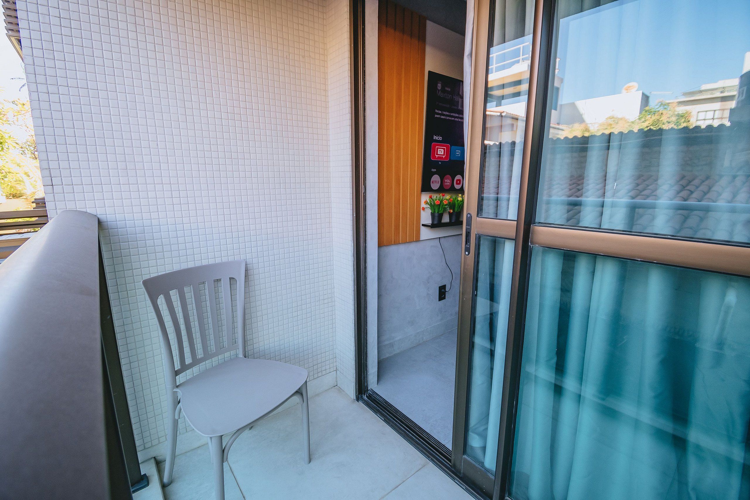 Un balcon avec une chaise blanche, une porte vitrée et un panneau de commande fixé au mur.