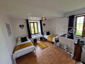 Een kamer met twee bedden, een raam met gordijnen, een nachtkastje met een lamp en een hangstoel.