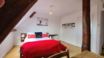 A bedroom with a wooden ceiling, a bed with red and white bedding, a hanging light fixture, and a white wall with a picture.