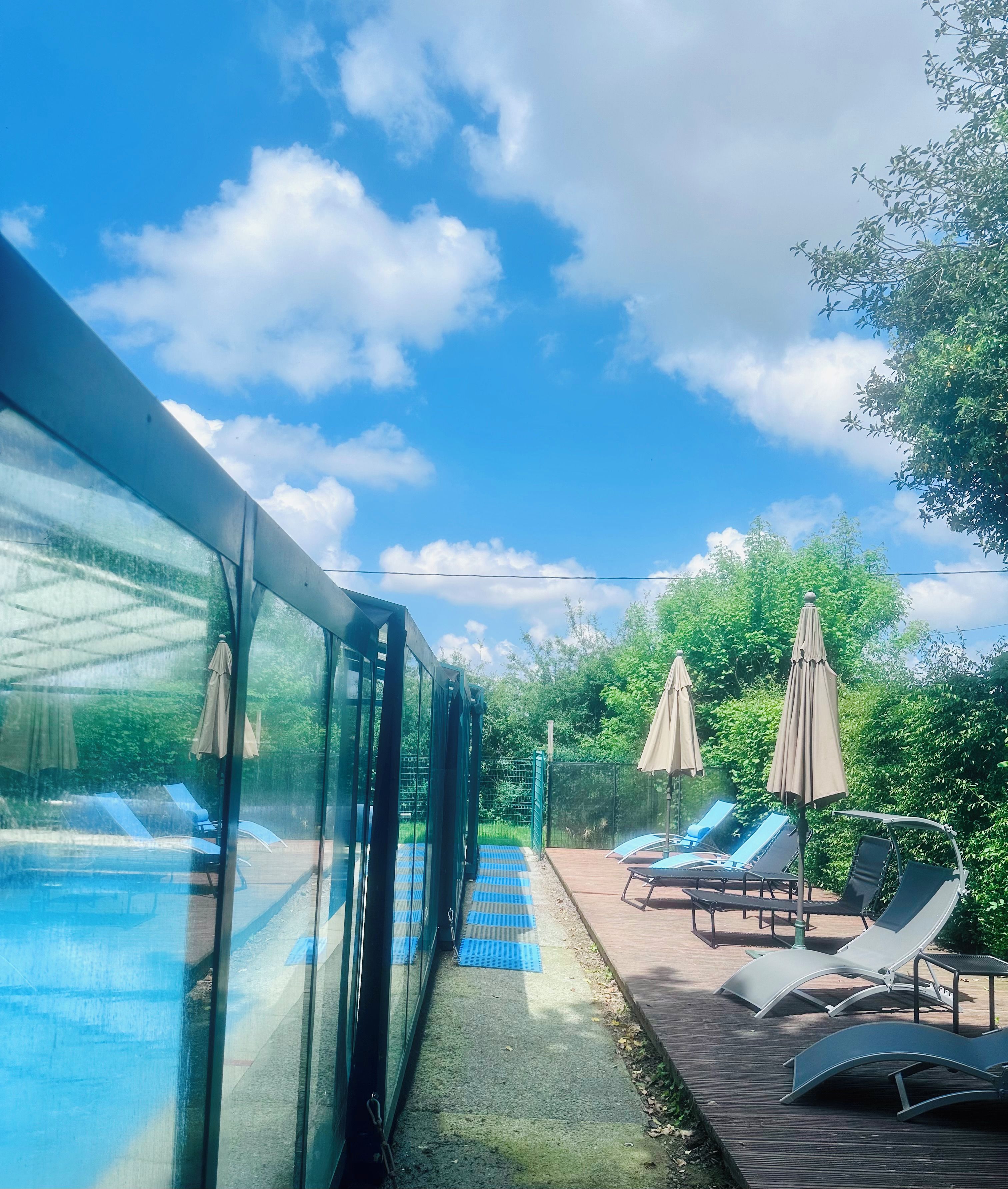 A poolside area with lounge chairs and umbrellas, a glass enclosure, and a wooden deck.