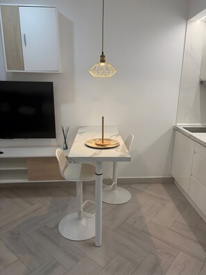 Una cocina moderna con una mesa de comedor, sillas, una lámpara colgante y un televisor.