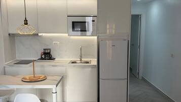 Una cocina moderna con armarios blancos, microondas integrado y refrigerador de acero inoxidable.