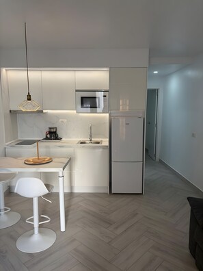 Una cocina moderna con armarios blancos, microondas integrado y refrigerador de acero inoxidable.