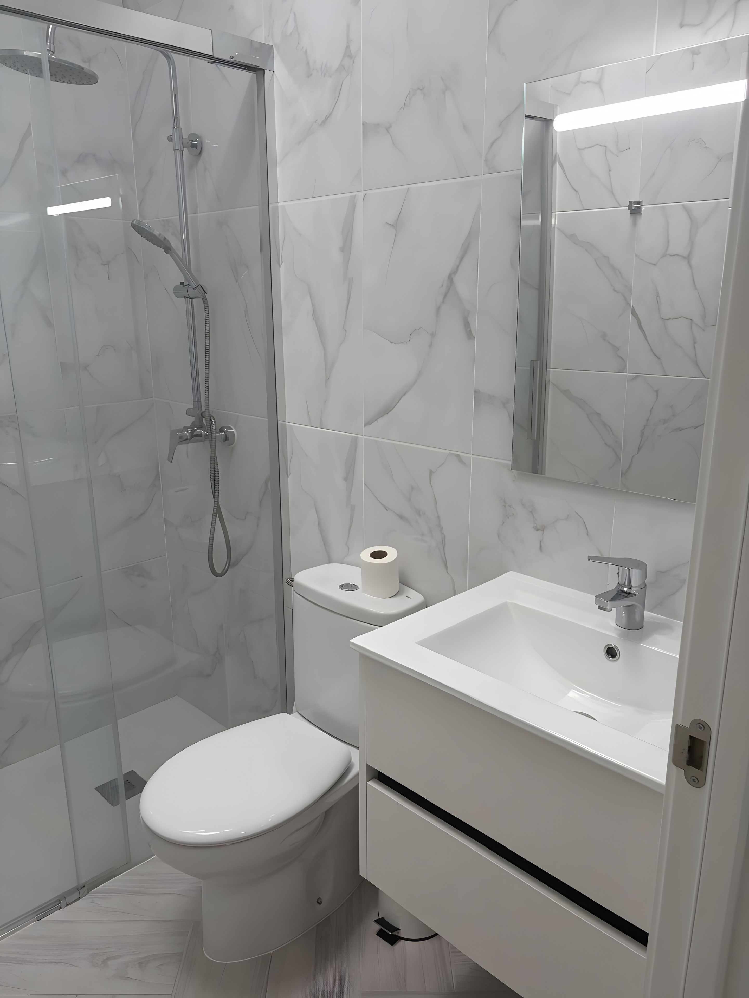 A modern bathroom with a glass-enclosed shower, a toilet, and a sink with a mirror above it.
