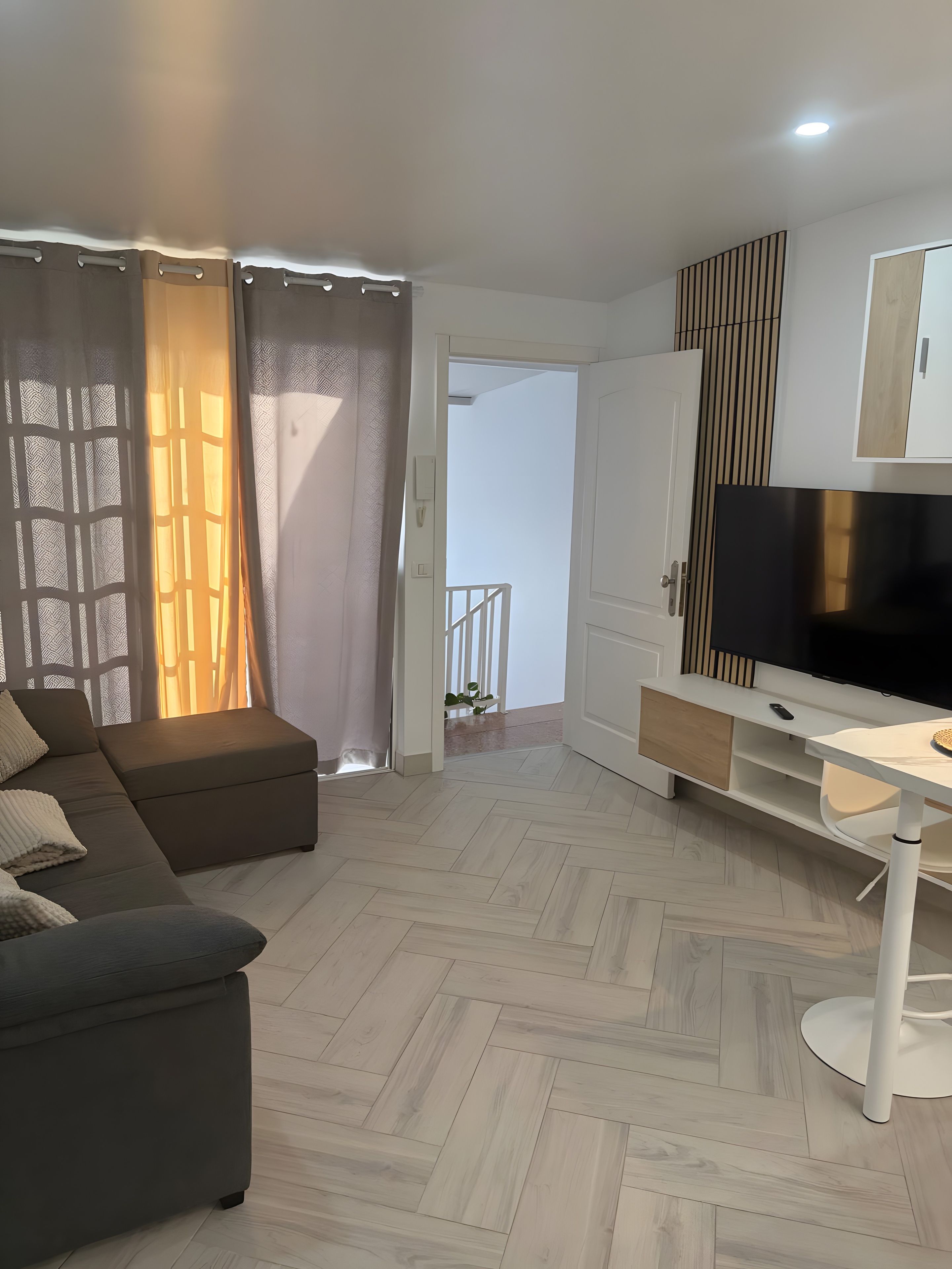 Een moderne woonkamer met een bank, een televisie en een visgraatvloer.