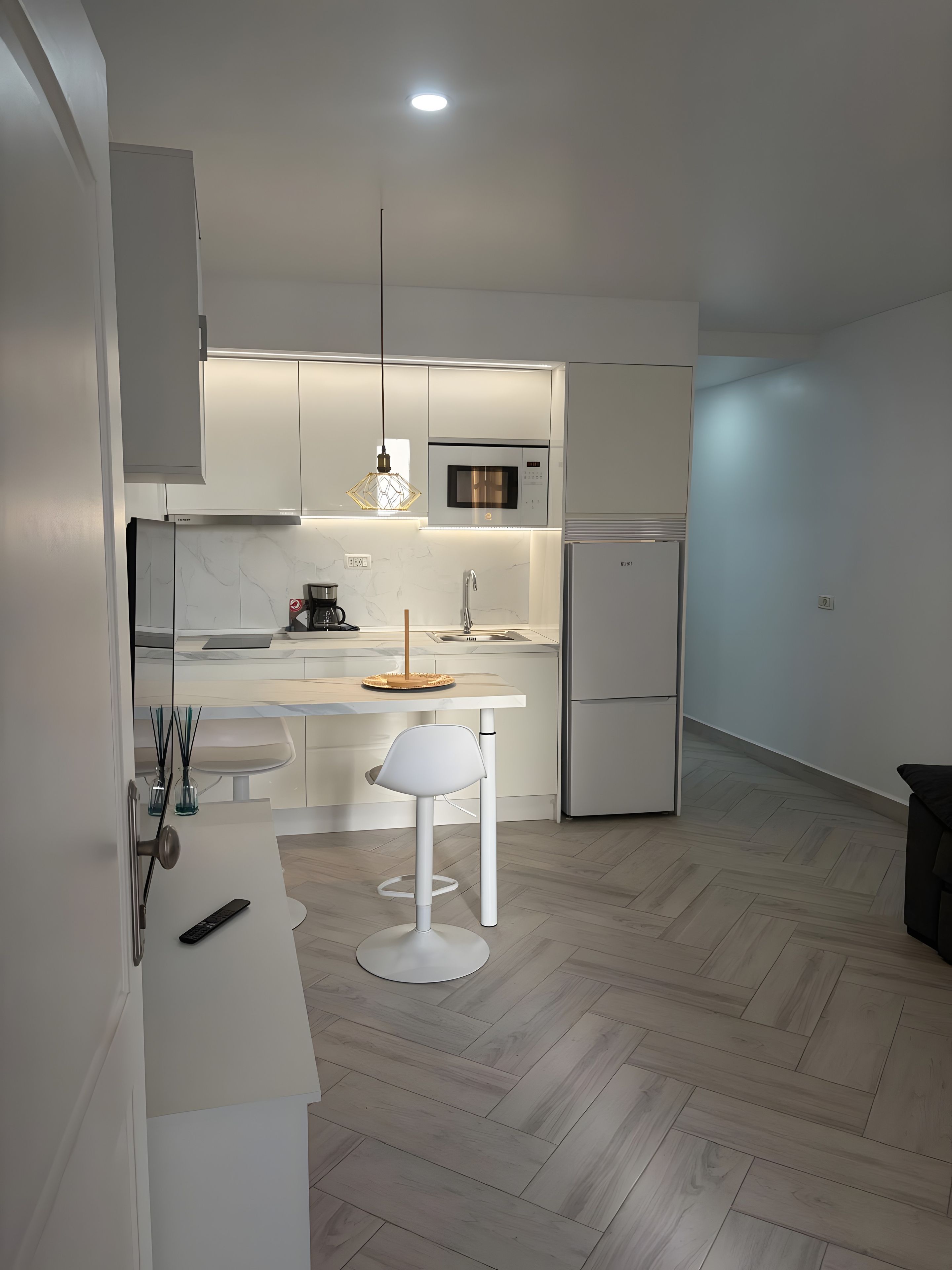Een moderne keuken met een magnetron, koelkast en een eethoek met een witte tafel en stoel.