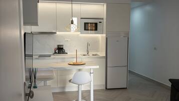 Een moderne keuken met een magnetron, koelkast en een eethoek met een witte tafel en stoel.