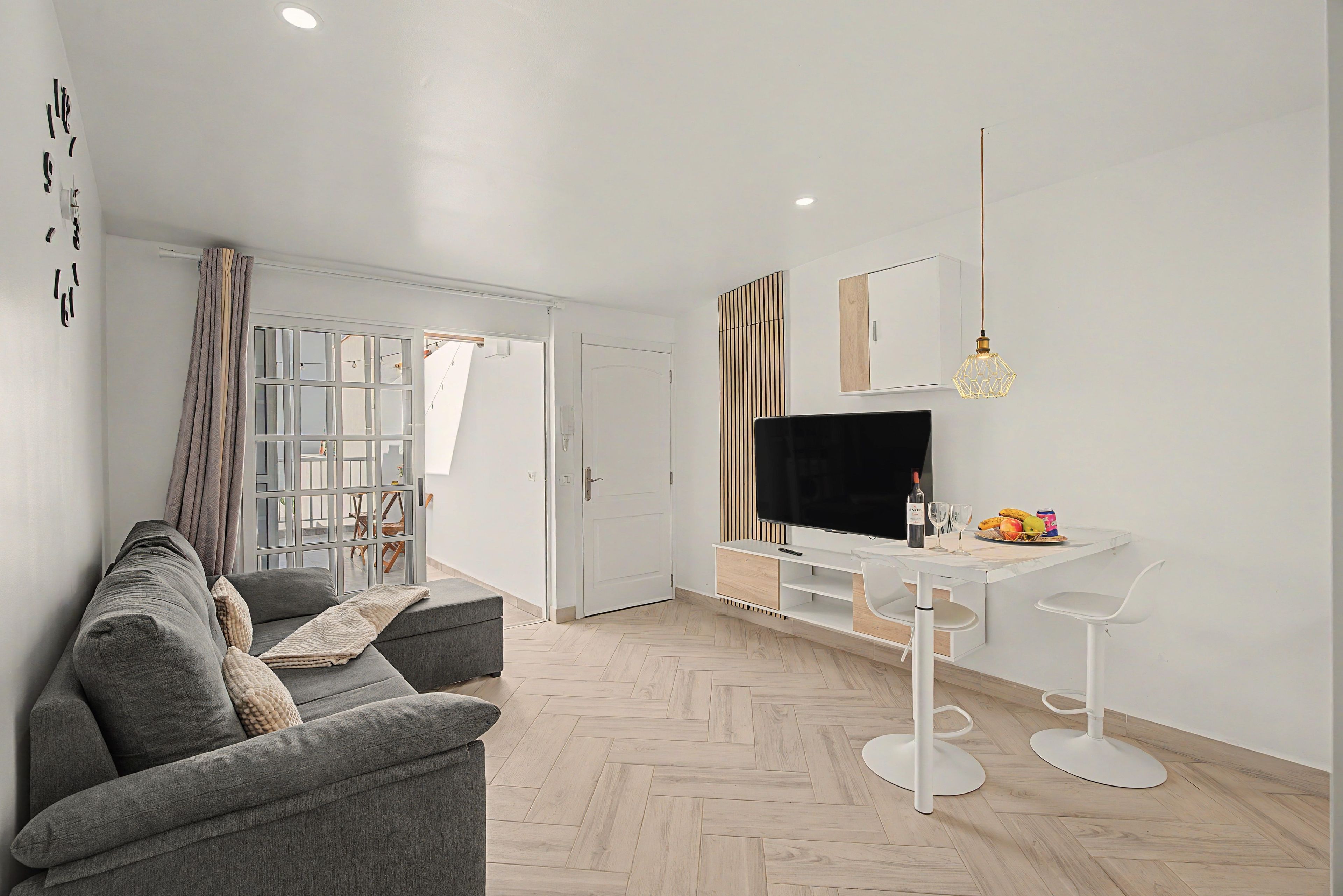 A modern living room with a grey sofa, a TV on a white stand, and a dining area with a white table and chairs.