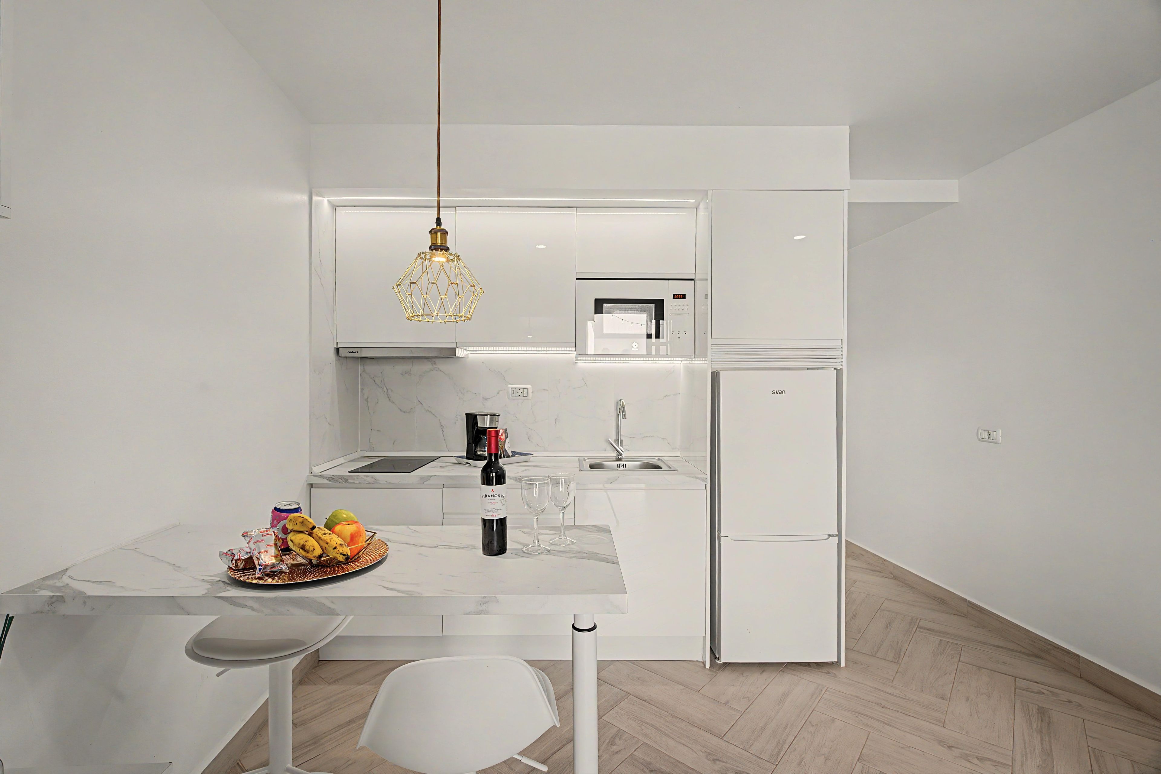 A modern kitchen with white cabinetry, a built-in oven, a coffee machine, and a refrigerator.