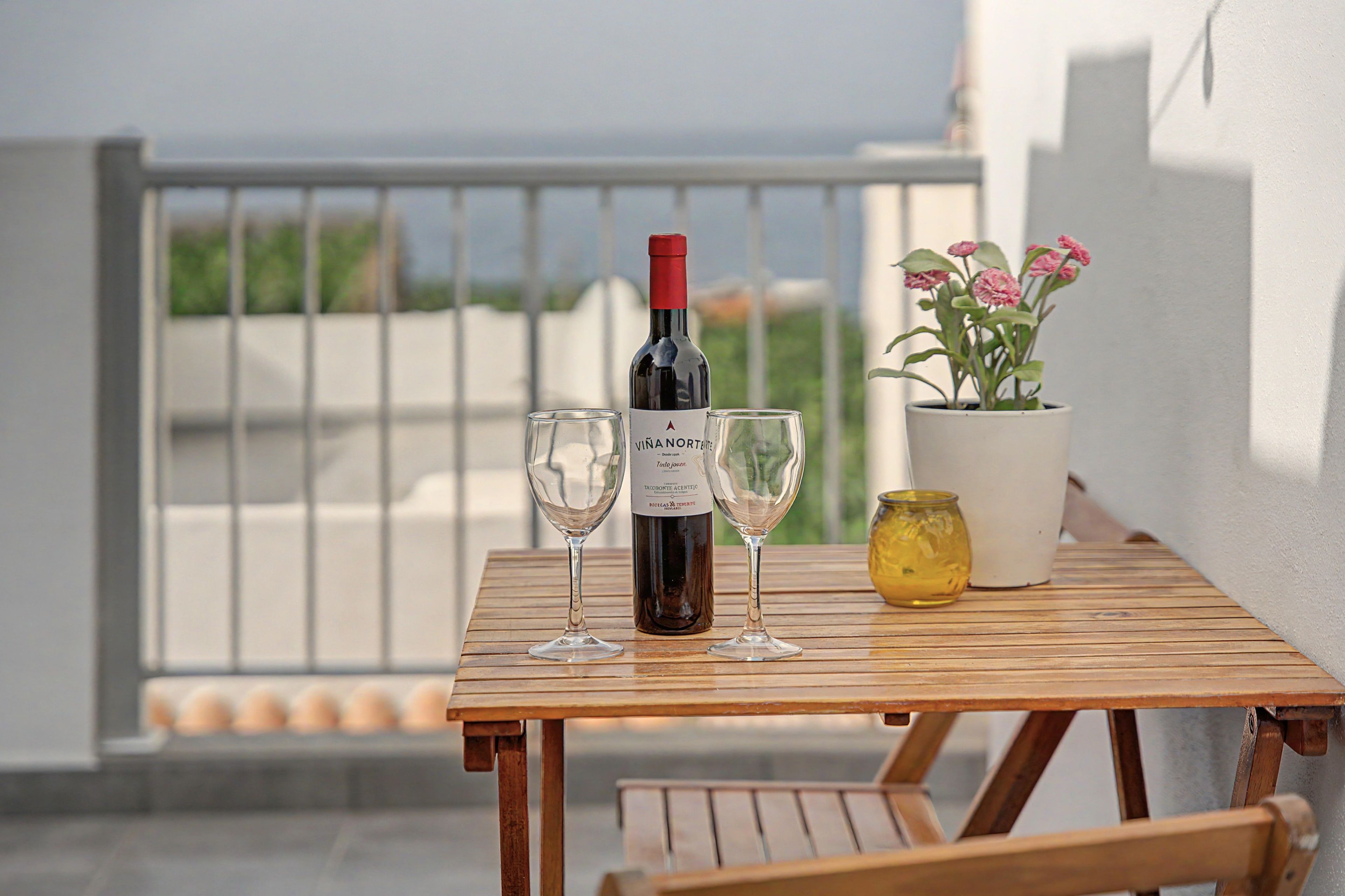 Uma garrafa de vinho, duas taças e um vaso com planta sobre uma mesa de madeira.