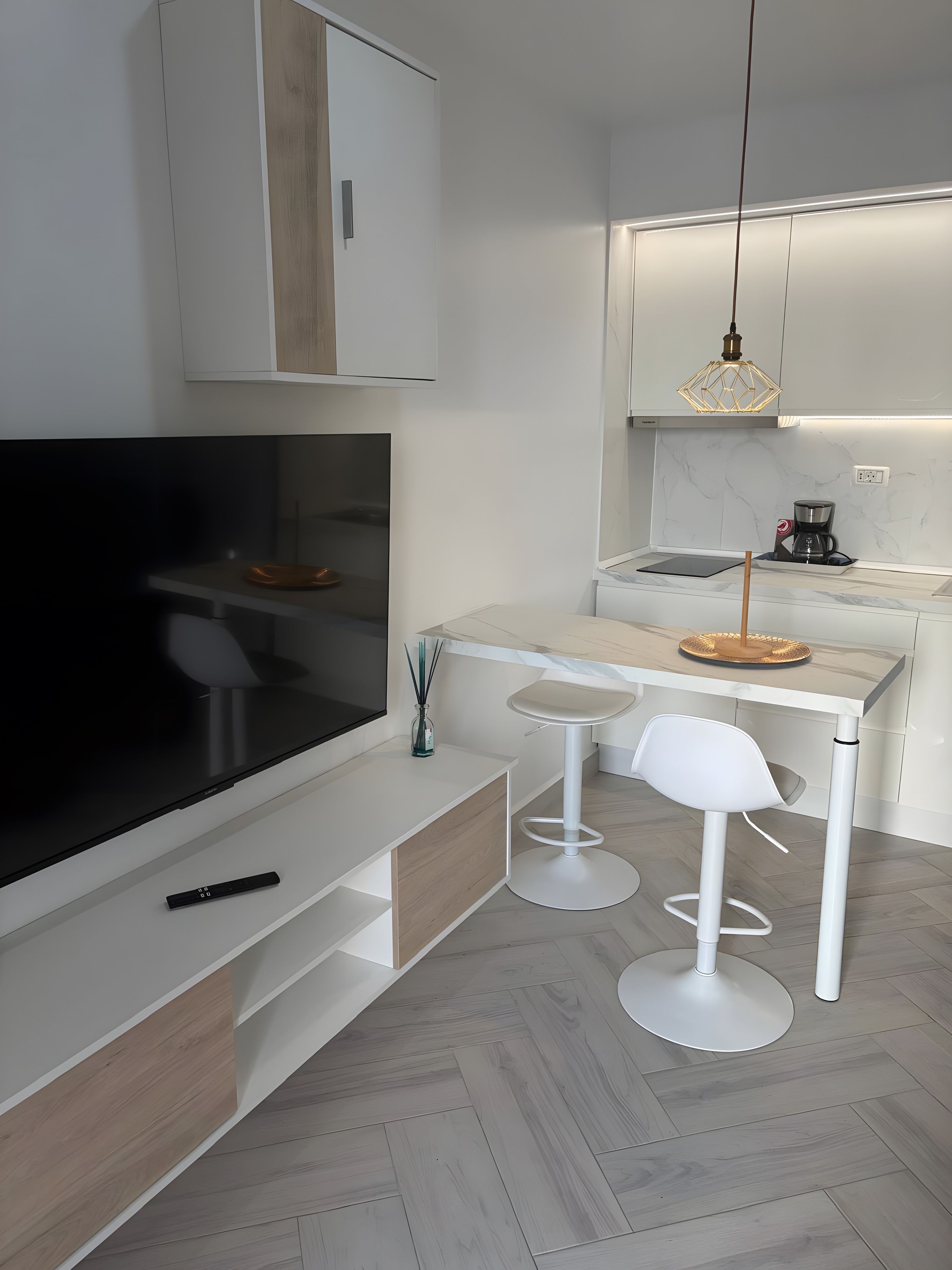 Una cucina moderna con TV integrata, sgabelli da bar bianchi e una macchina per il caffè.