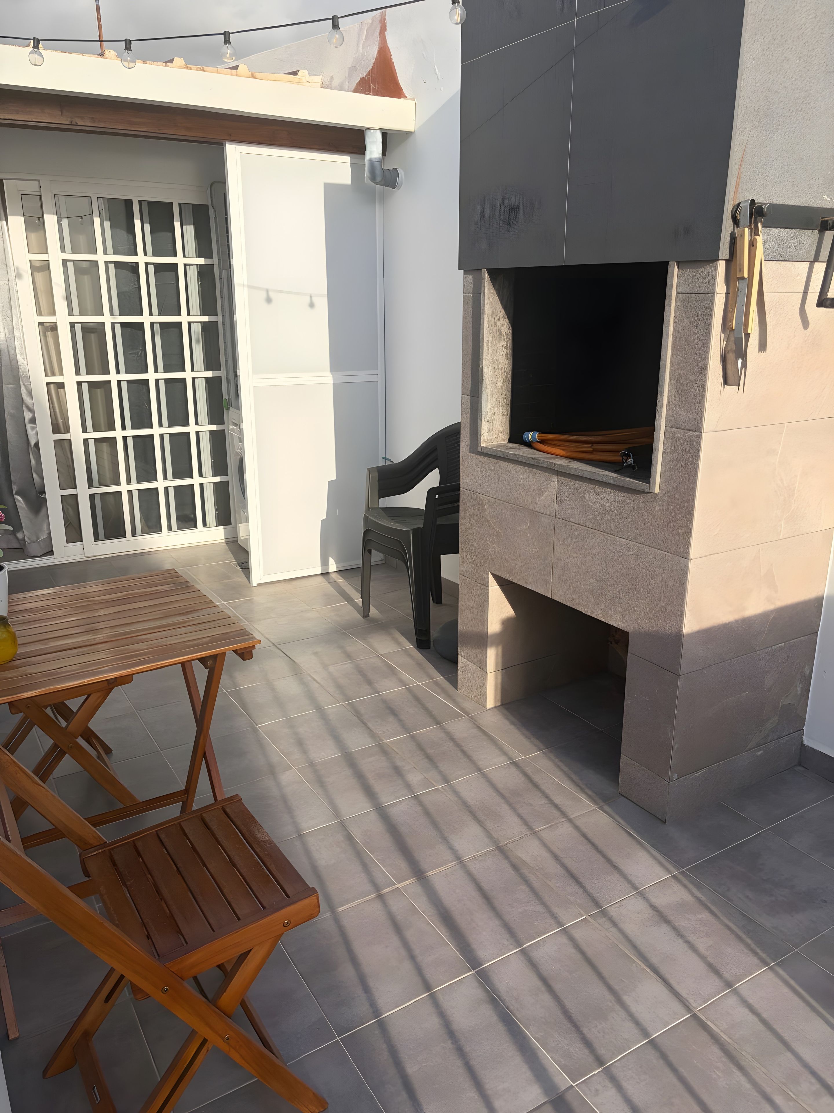 A patio with a barbecue grill, a folding table, and a chair.