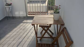 Una terraza en la azotea con mesa y sillas de madera, plantas en macetas y vistas al mar.