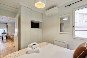 Ett hotellrum med en säng, en tv som är monterad på väggen, ett fönster och en luftkonditioneringsanläggning.