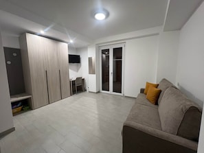 A modern living room with a sofa, a TV mounted on the wall, and a sliding glass door leading to a balcony. - A un Passo dalla Piazza (San Giovanni Gemini)
