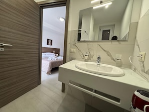 A modern bathroom with a large mirror, a white sink, and a marble backsplash. - A un Passo dalla Piazza (San Giovanni Gemini)