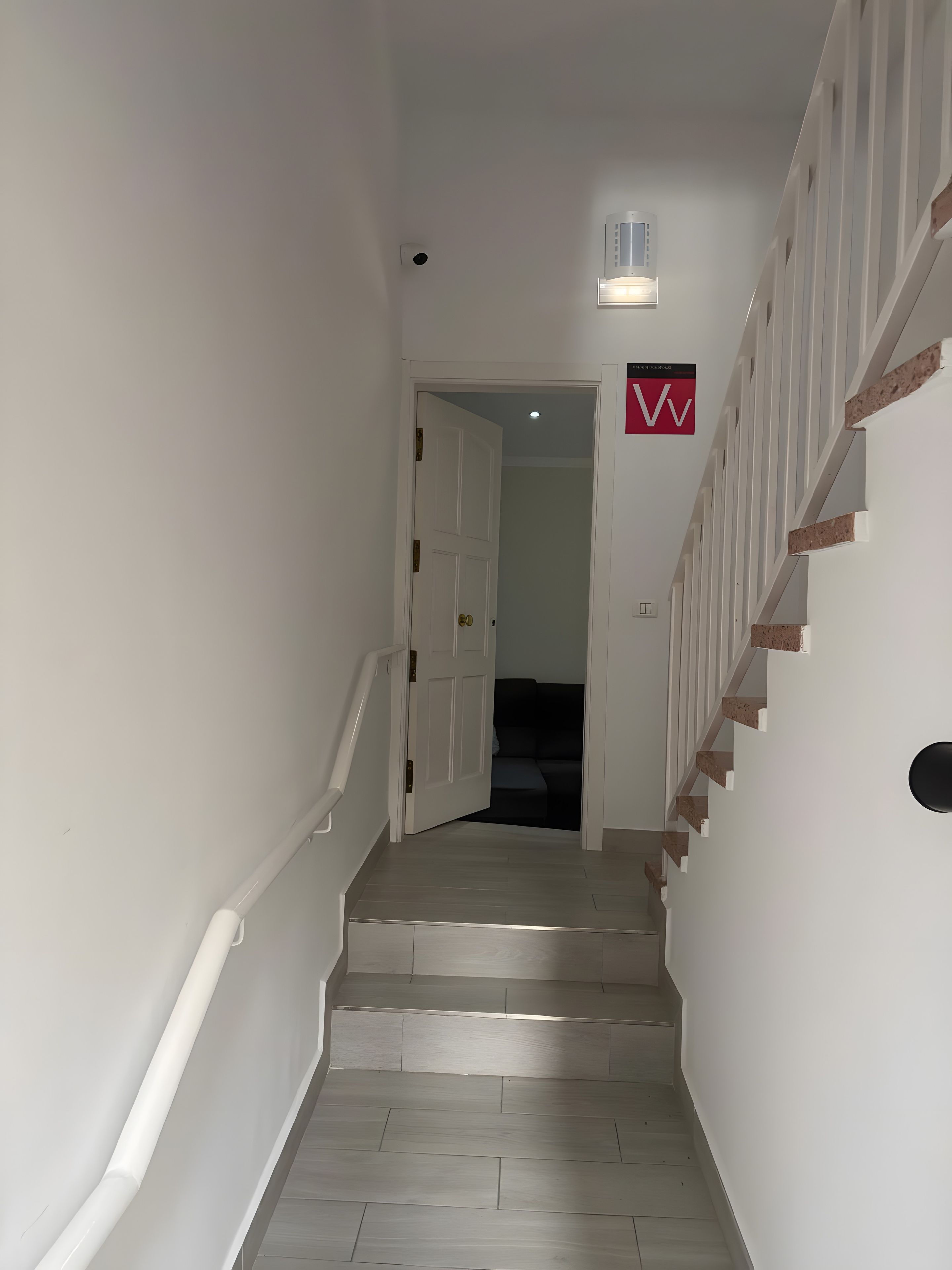 Un escalier avec une rampe, un luminaire au-dessus et une porte donnant sur une autre pièce.