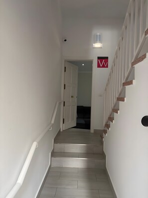Un escalier avec une rampe, un luminaire au-dessus et une porte donnant sur une autre pièce.