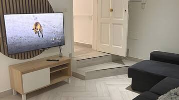 A modern living room with a flat-screen TV on a wooden console, a dark sofa, and a herringbone-patterned floor.