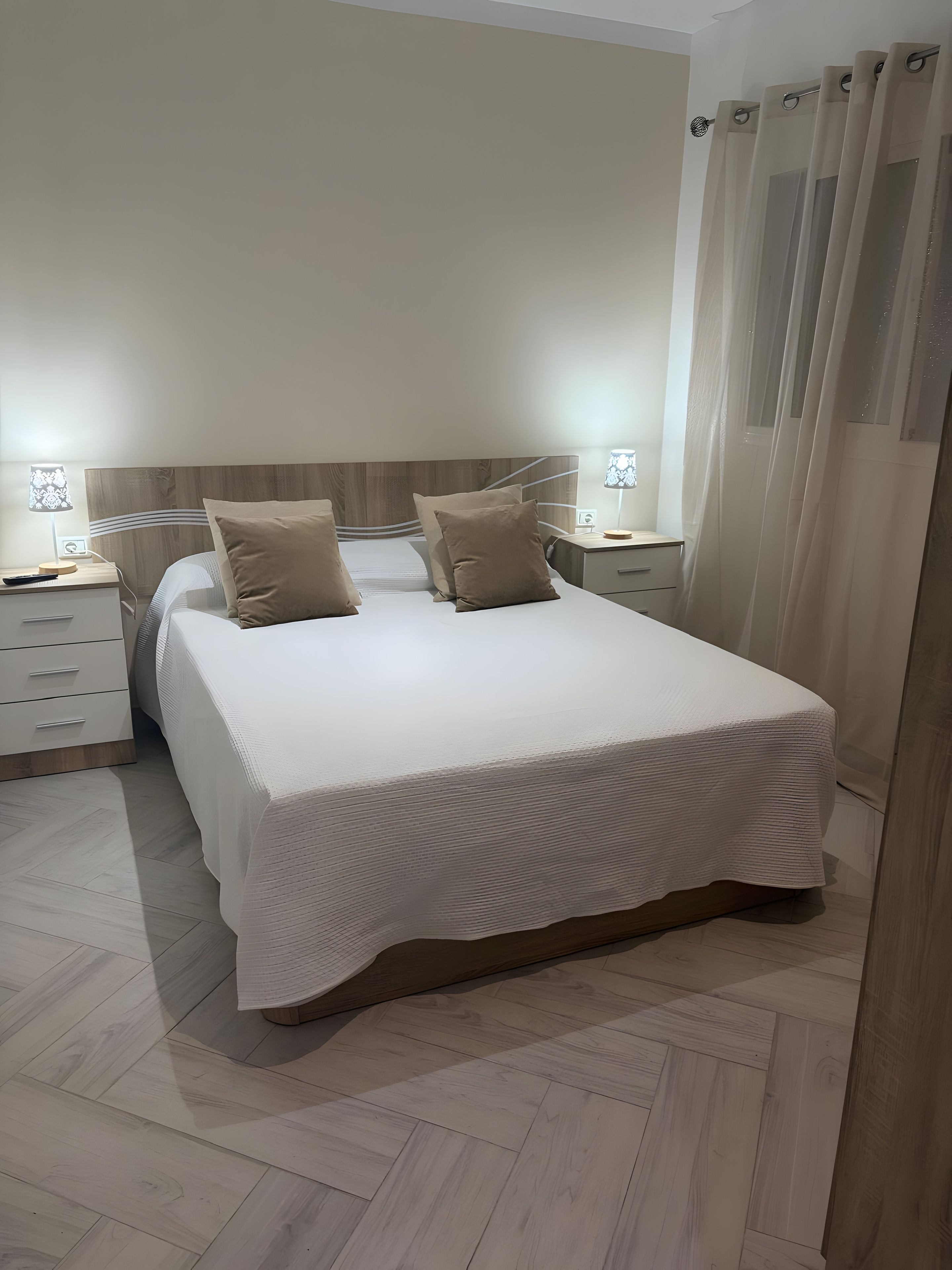 A bedroom with a large bed, two bedside tables, a nightstand, and a window with curtains.