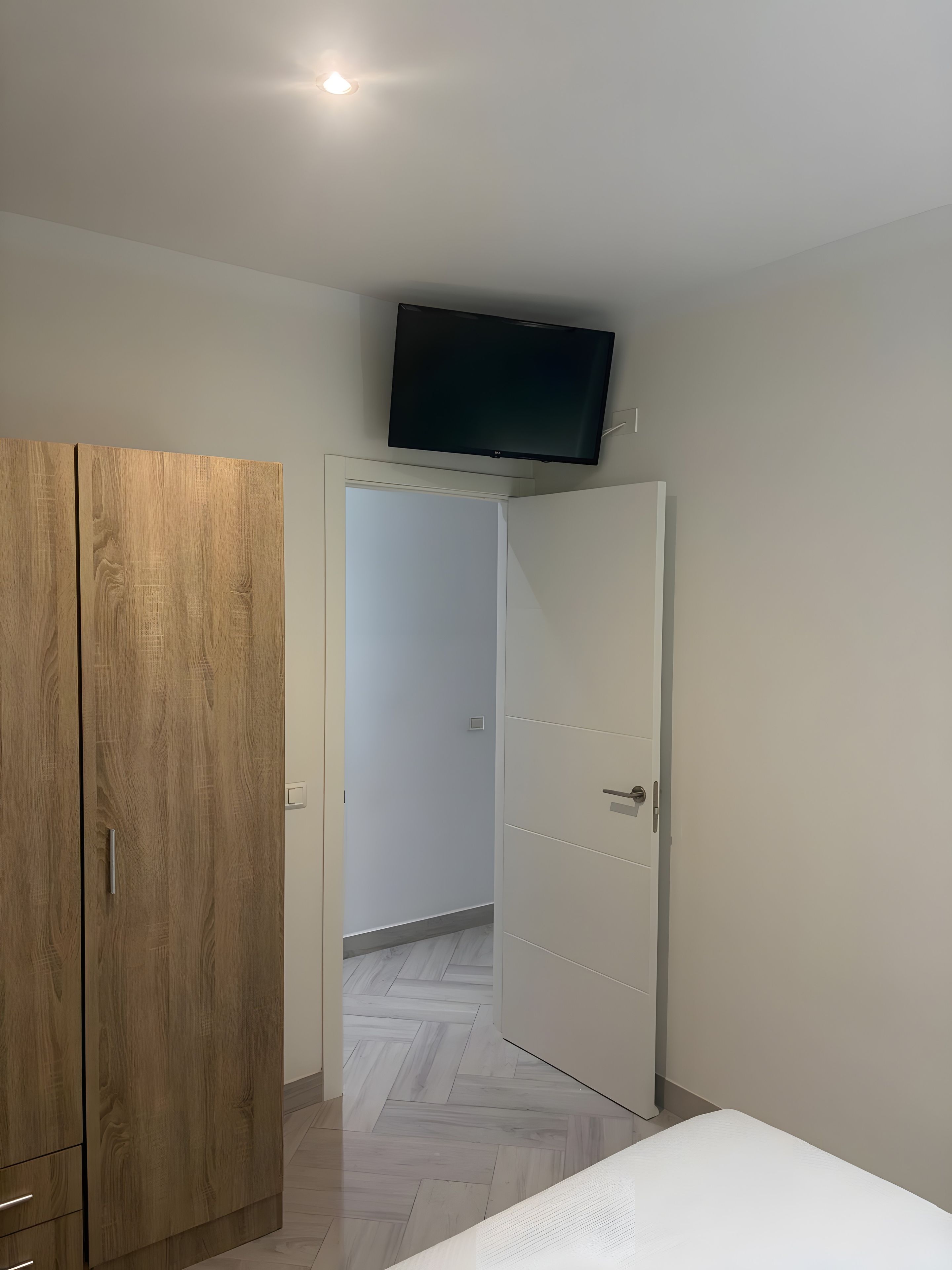 A bedroom with a wooden wardrobe, a bed, and a television mounted on the wall.
