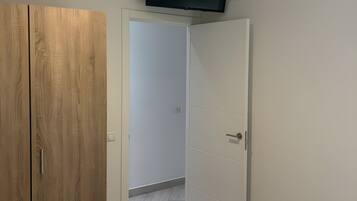 A bedroom with a wooden wardrobe, a bed, and a television mounted on the wall.