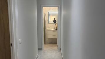 A hallway with a herringbone floor pattern leading to a bathroom with a mirror, sink, and toilet.