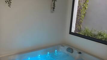 Een wellnessruimte met een jacuzzi, plantenbakken en een raam met beplanting.