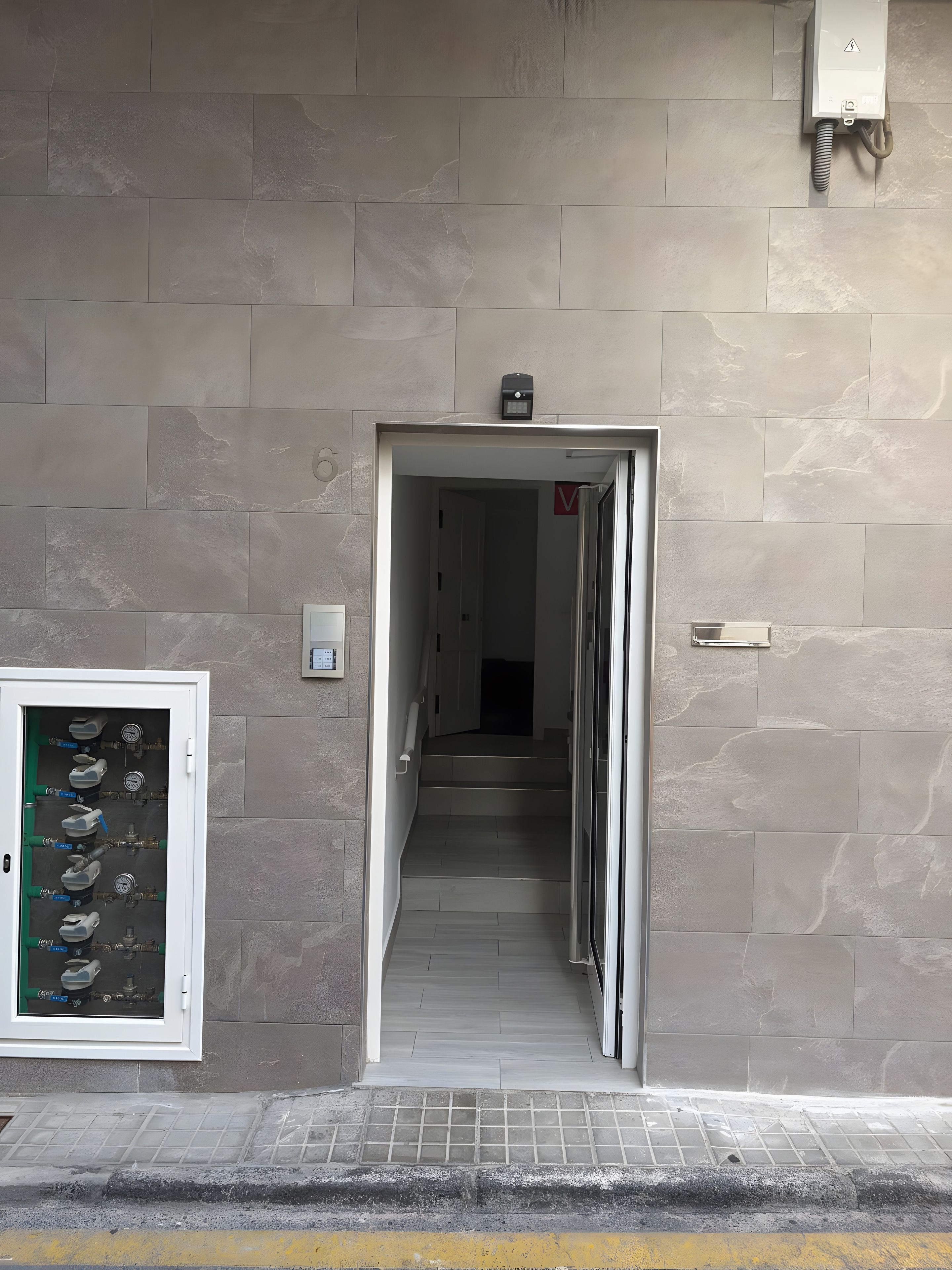 A hallway leading to a staircase with a water meter on the wall.