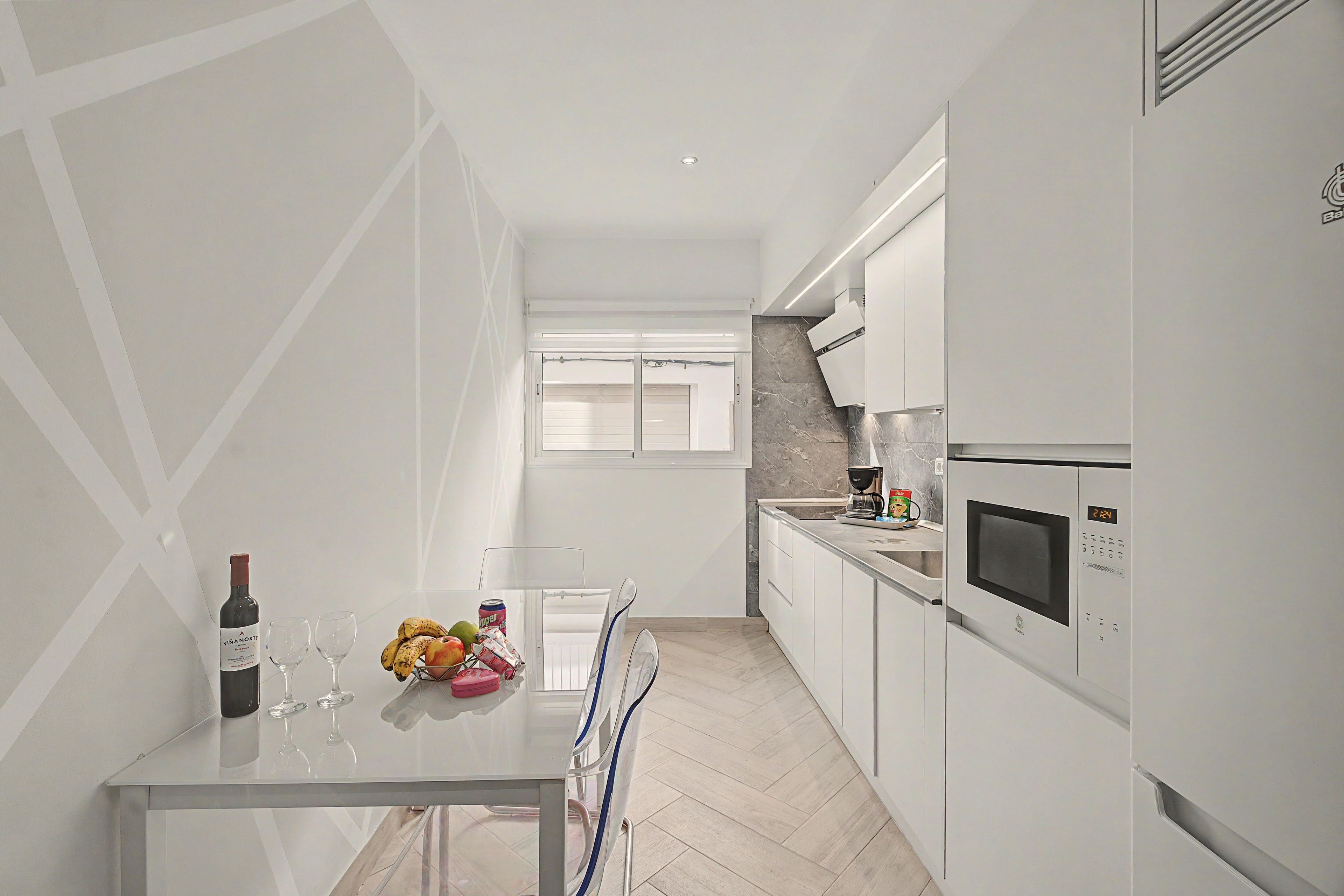 A modern kitchen with white cabinetry, a built-in microwave, and a dining area with a glass table.