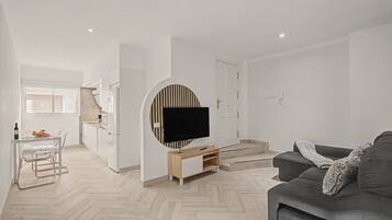 A modern living room with a grey sofa, a flat-screen TV mounted on a wall, and a herringbone-patterned wooden floor.