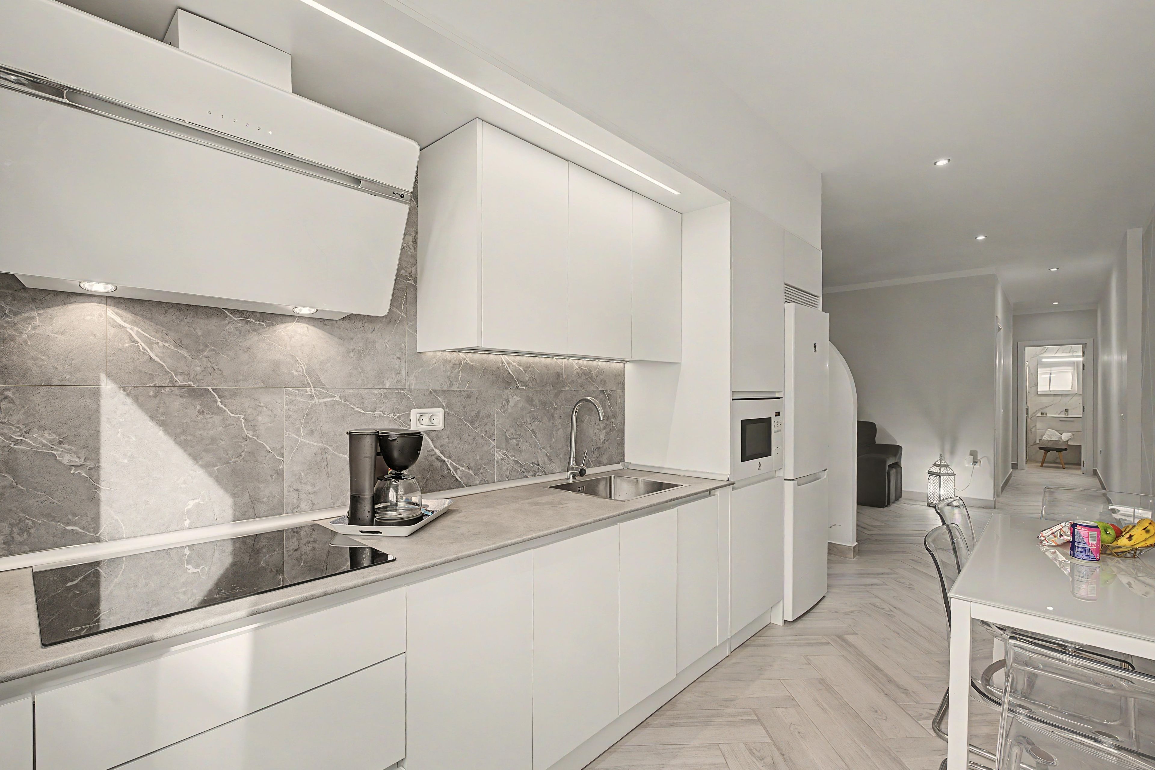 A modern kitchen with white cabinetry, a marble backsplash, and a built-in oven.