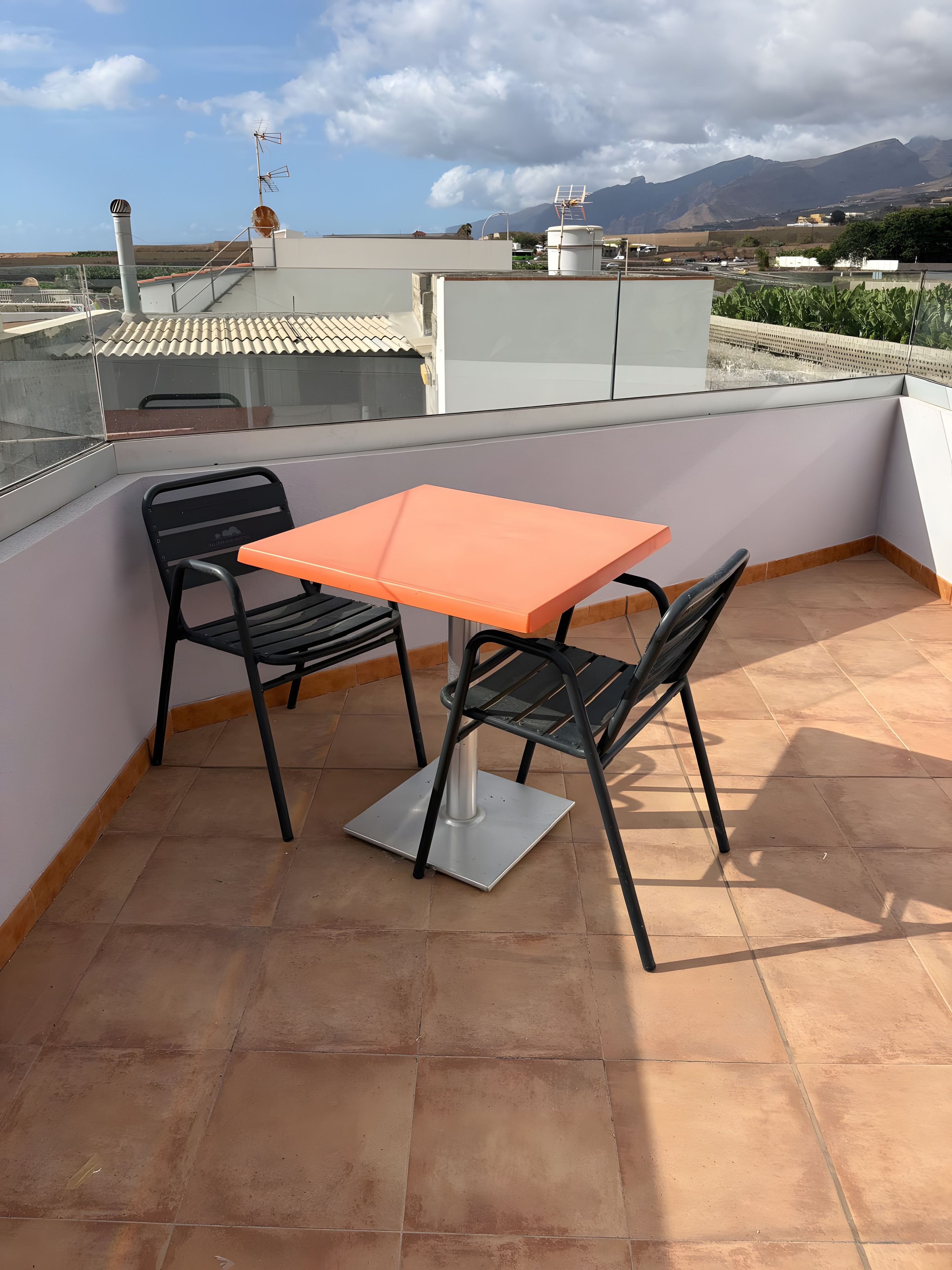 A rooftop terrace with a table and chairs, a clear view of the surrounding landscape, and a water tank in the background.